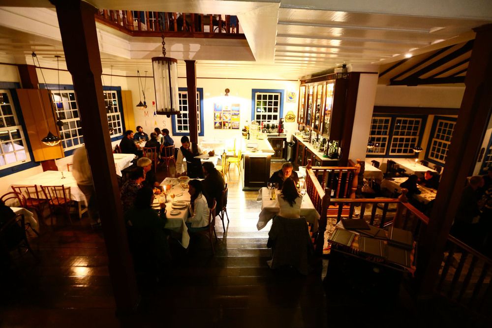Ambiente interno de restaurante colonial em Ouro Preto, com mesas ocupadas por pessoas jantando e decoração em estilo antigo